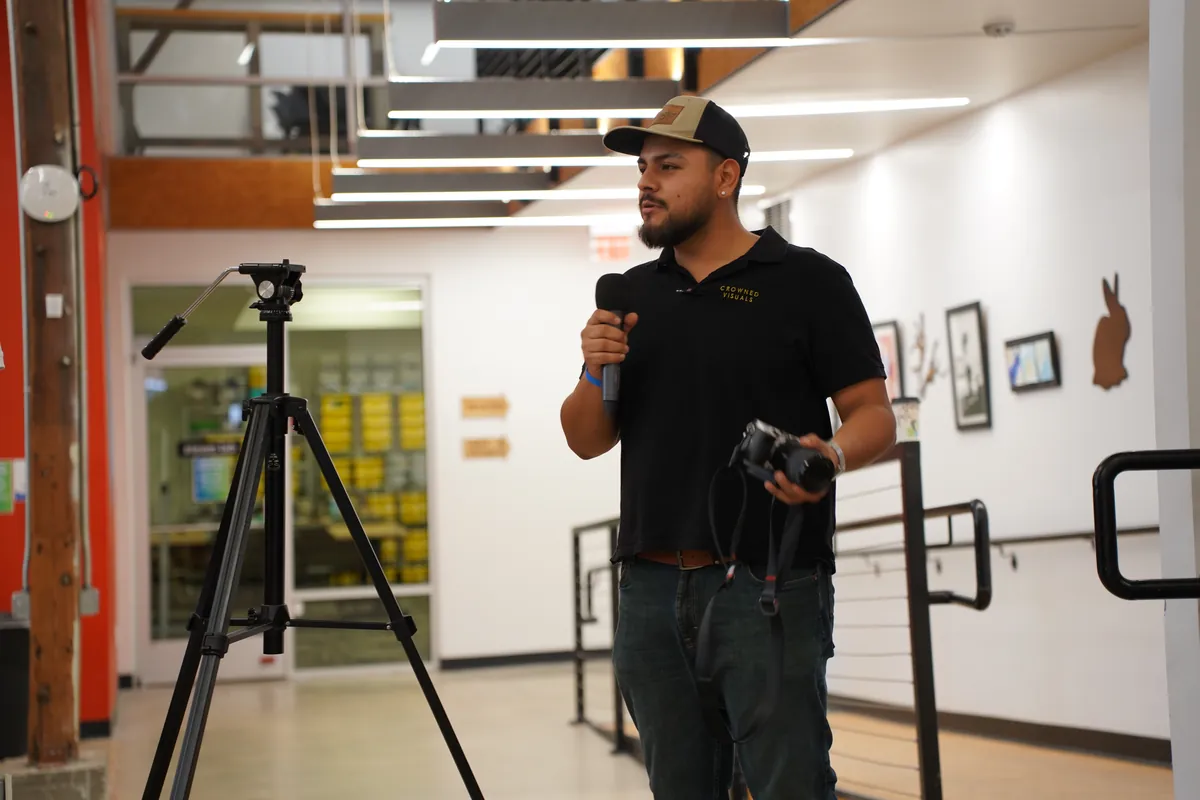 A volunteer photographer speaking beside a camera tripod at ARKAST 2025
