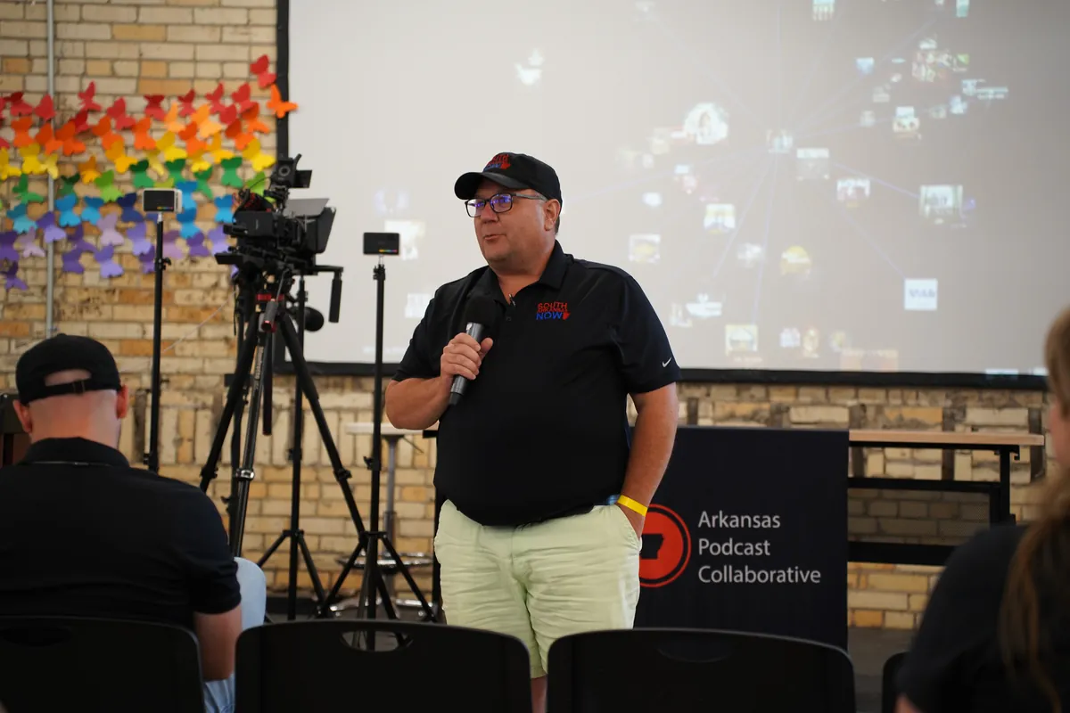 Speaker at the podium beside the Arkansas Podcast Collaborative sign at ARKAST 2025